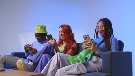 Studio-Shot-Of-Group-Of-Young-Gen-Z-Friends-Sitting-On-Sofa-Gaming-And-Using-Social-Media-On-Mobile-Phones